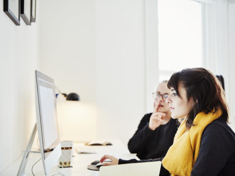 Two women seated sharing a computer screen and discussing the graphic content.